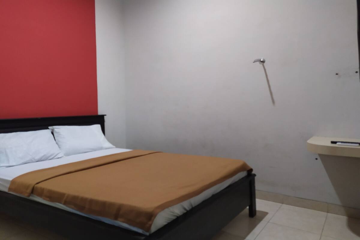A bed with white and brown bedding, a red wall, and a white ceiling.