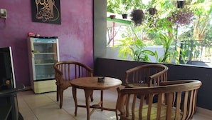 A room with a purple wall, a glass display case, wooden chairs, a small table, and a window with plants outside. - OYO 2654 Yulia Guesthouse Near Kopi Bajawa Flores NTT Tebet (Jakarta)