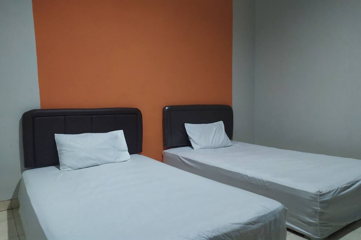 Two single beds with white linens in a room with an orange accent wall and a grey wall.