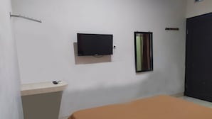 A bedroom with a bed, a TV mounted on the wall, a small bedside table, and a door. - OYO 2654 Yulia Guesthouse Near Kopi Bajawa Flores NTT Tebet (Jakarta)