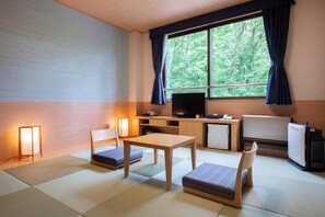 Una habitación con suelo de tatami, una mesa de madera, dos sillas, un televisor, un refrigerador y una ventana con cortinas.