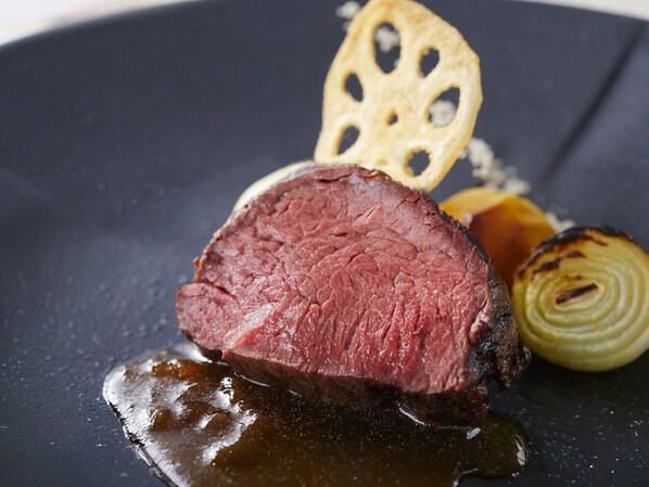 Un plat composé d’une tranche de viande, d’un légume rond et d’un morceau de pain plat, le tout présenté sur une assiette sombre.