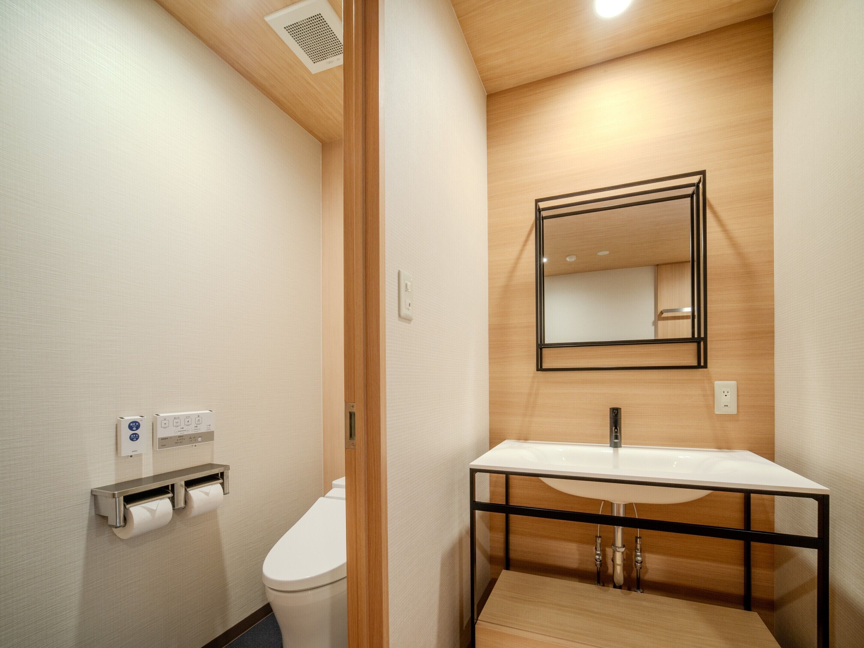 A modern bathroom with a toilet, a sink with a black frame, a mirror, and a paper towel dispenser.