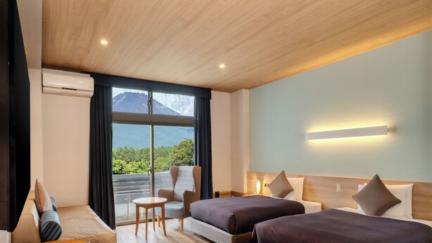 A hotel room with two beds, a sofa, a small table, and a view of a mountain. - Wan Wan Paradise Premier Yamanakako (Yamanakako)