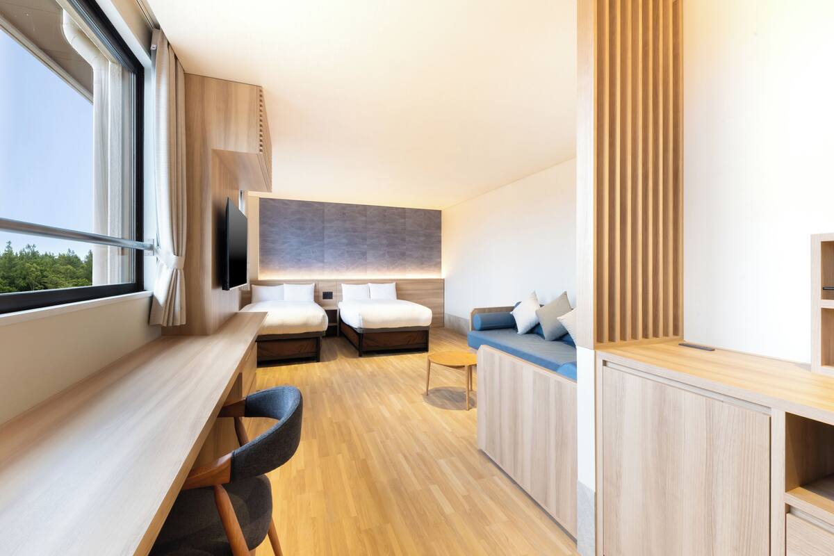 Een moderne hotelkamer met houten vloer, twee bedden, een bureau, een televisie en uitzicht op de omgeving.