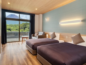 A hotel room with two beds, a sofa, a small table, and a view of a mountain through a large window.