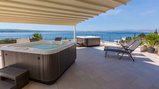 Une terrasse sur le toit avec un jacuzzi, des chaises longues et une vue sur la mer.