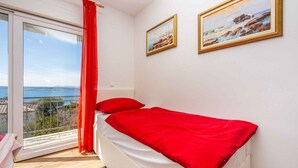 Une chambre à coucher avec un lit, une fenêtre donnant sur la mer et deux tableaux accrochés au mur.