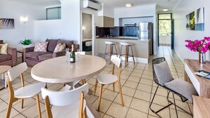Una sala de estar moderna con una mesa de comedor redonda, sillas blancas, un sofá y una zona de cocina con barra.