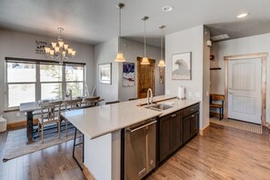 A modern kitchen with a large island, pendant lights, and a view of the outdoors.