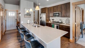 A modern kitchen with a large island, bar stools, stainless steel appliances, and pendant lighting.