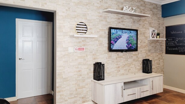 En moderne reception med væg i stengulvsmønster, et fladskærms-tv, et skilt med 'Relax', en hvid konsol og en tavle med information om Wi-Fi.