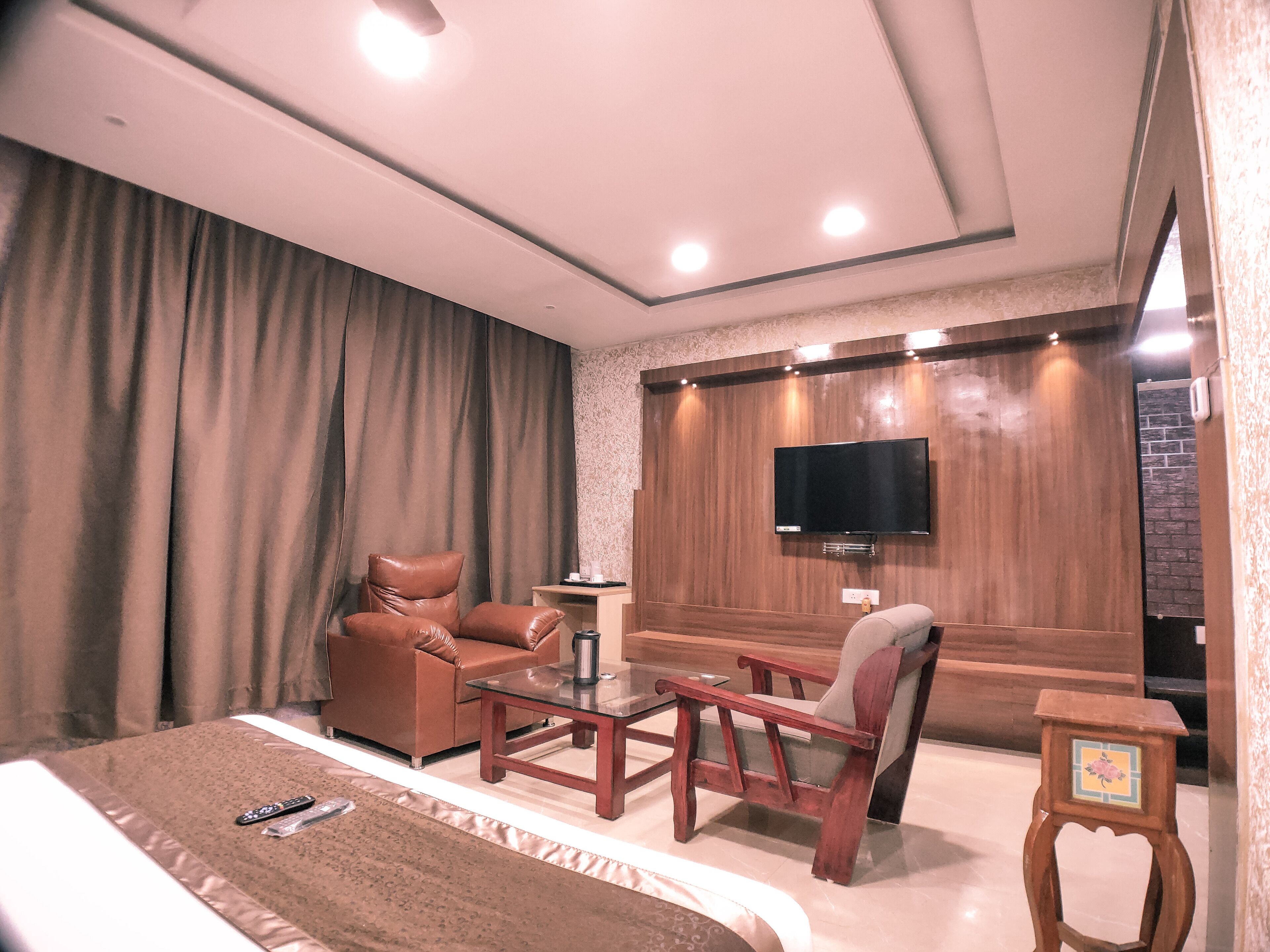 A hotel room with a bed, two sofas, a coffee table, a TV mounted on the wall, and a small table with a decorative item.
