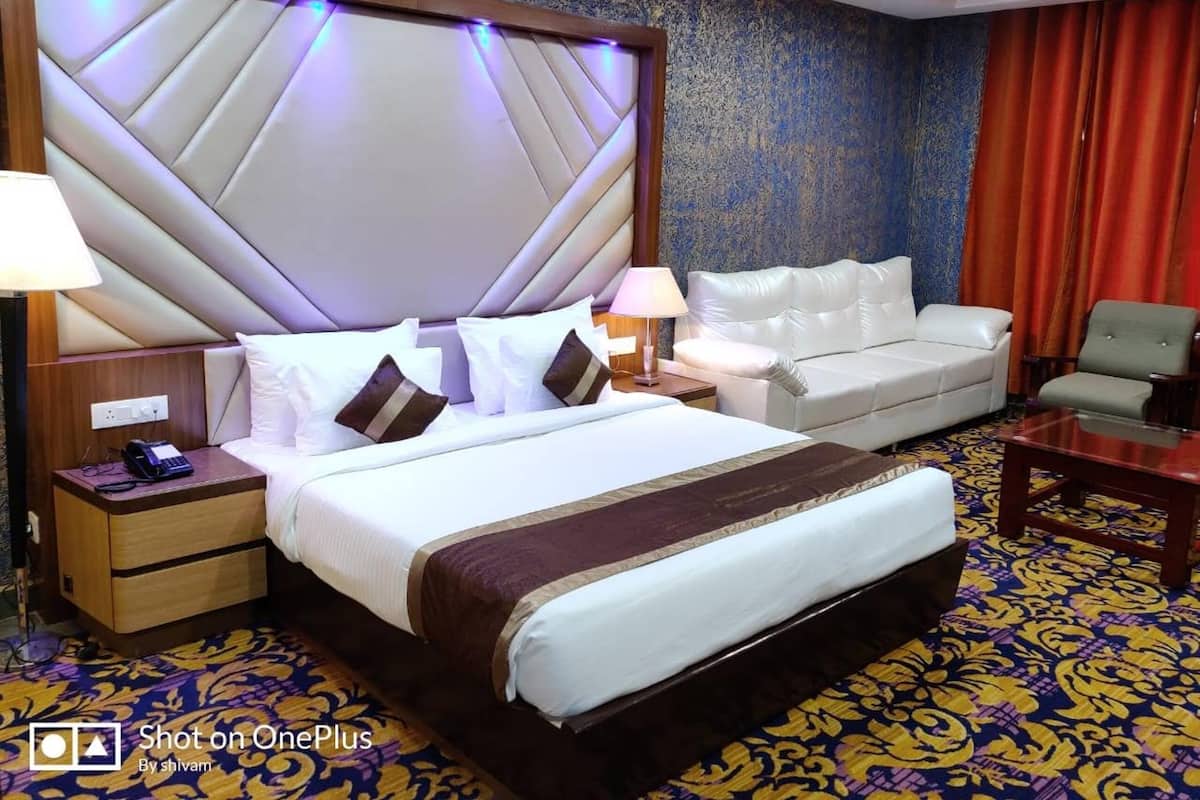 A hotel room with a large bed, a sofa, a chair, and a small table.