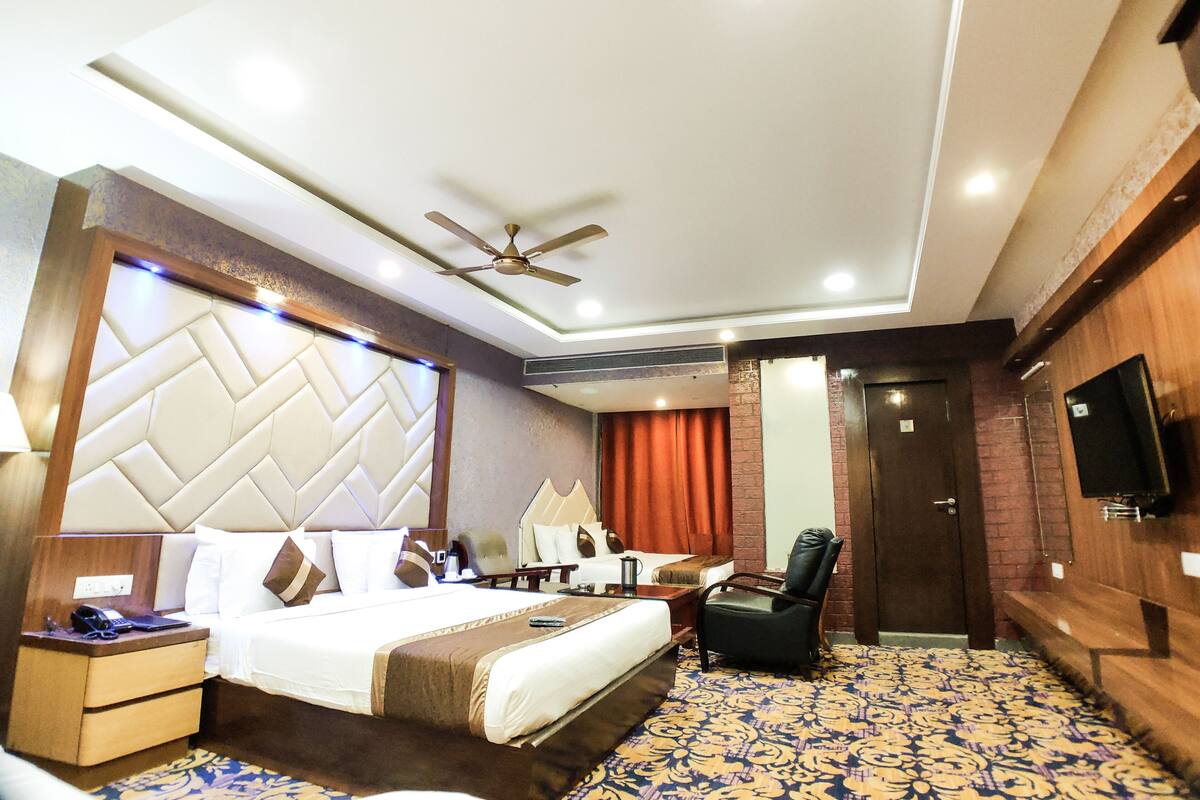 A hotel room with a bed, bedside table, chair, TV, and a ceiling fan.
