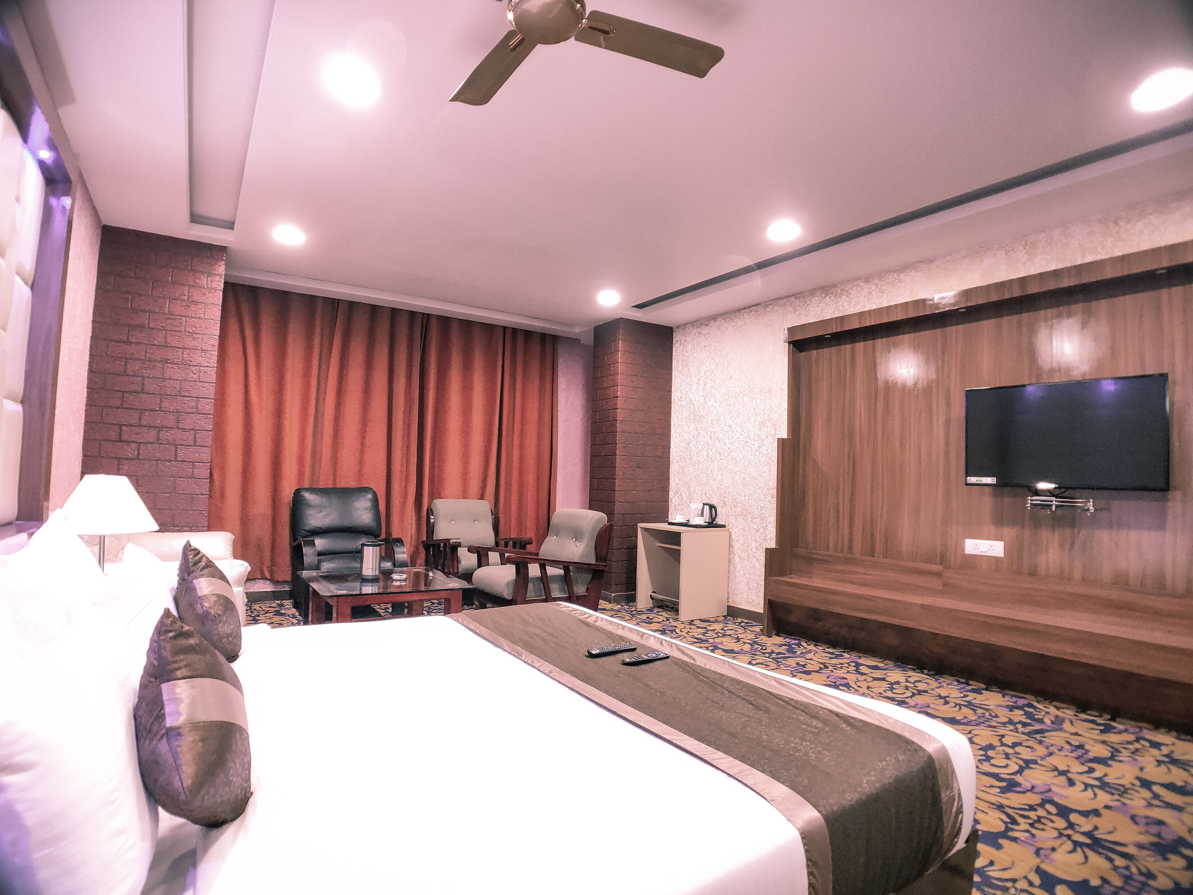 A hotel room with a bed, a desk, a TV, and a ceiling fan.