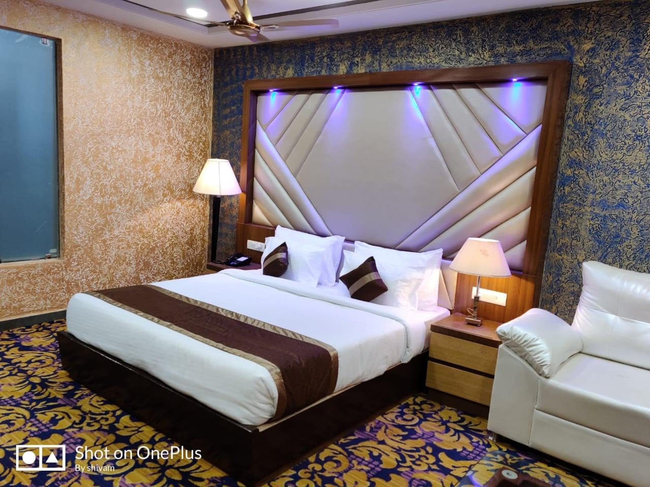 A hotel room with a large bed, a nightstand, a chair, and a patterned carpet.