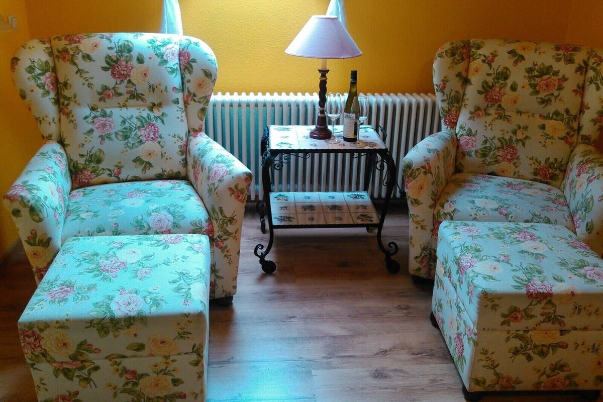Une pièce comprenant deux fauteuils à motifs floraux, une petite table avec une lampe et un radiateur.