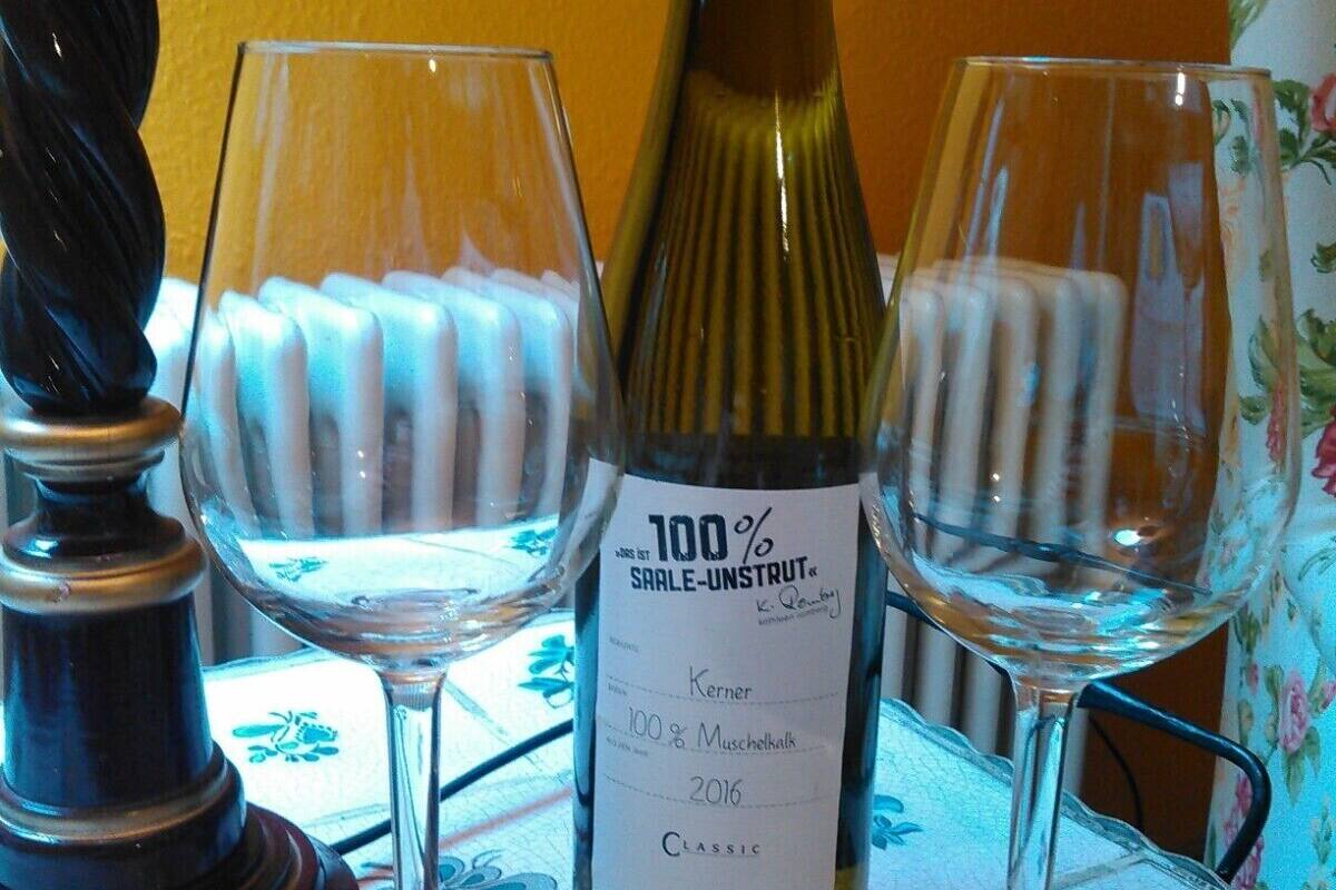 Une bouteille de vin 100 % Muschelkalk, millésime 2016, est posée sur une table, accompagnée de deux verres à vin.