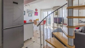 Una cucina moderna con un frigorifero in acciaio inossidabile, una zona pranzo con una sedia rossa e una scala che conduce a un soggiorno con un divano.