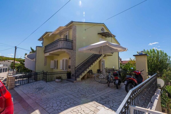 Una casa de dos pisos con un balcón, una escalera y un patio cubierto.
