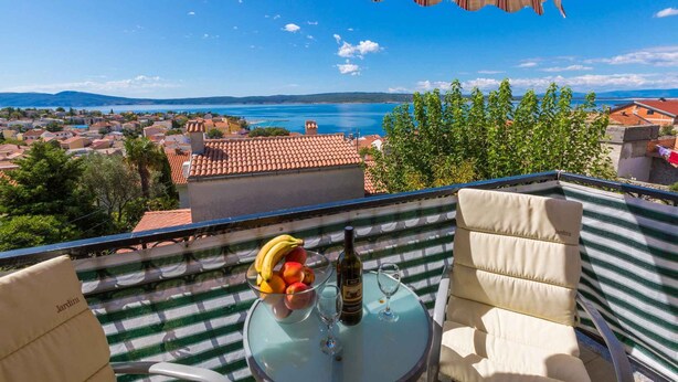 Un balcone con tavolo, due sedie, una ciotola di frutta, una bottiglia di vino e un bicchiere.