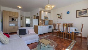 A compact living space with a kitchenette, a dining area with wooden chairs, a sofa, and a glass coffee table. - Holiday apartment mit Klimaanlage und Balkon (Selce)