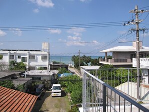 Zona residencial con un edificio blanco, una camioneta blanca estacionada y vista al mar.