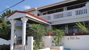 A two-story building with a white facade, a red roof, and a balcony. There is a sign on the building that reads "Hibis Yabu". - Hibisu yabu (Nago)