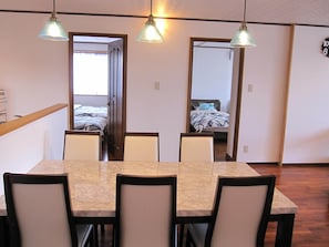 A dining area with a marble table and chairs, a wooden ceiling, and a bed visible through an open door. - Hibisu yabu (Nago)