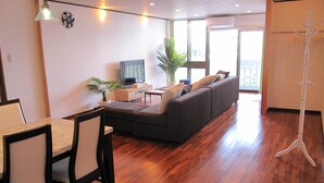 A living room with a sofa, a TV, a dining table with chairs, and a plant. - Hibisu yabu (Nago)