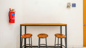 A room with a wooden table and three stools, a fire extinguisher mounted on the wall, and a door with a handle. - Hotel O Syariah Tasikmalaya Near Universitas Siliwangi Formerly Siliwangi Guest House (Tasikmalaya)