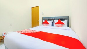 A neatly made bed with a red and white bedspread, a wooden door, and a small table with a box on it. - Hotel O Syariah Tasikmalaya Near Universitas Siliwangi Formerly Siliwangi Guest House (Tasikmalaya)