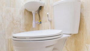 A white toilet with a tank and a wall-mounted sink in a bathroom with marble tiles. - Hotel O Syariah Tasikmalaya Near Universitas Siliwangi Formerly Siliwangi Guest House (Tasikmalaya)