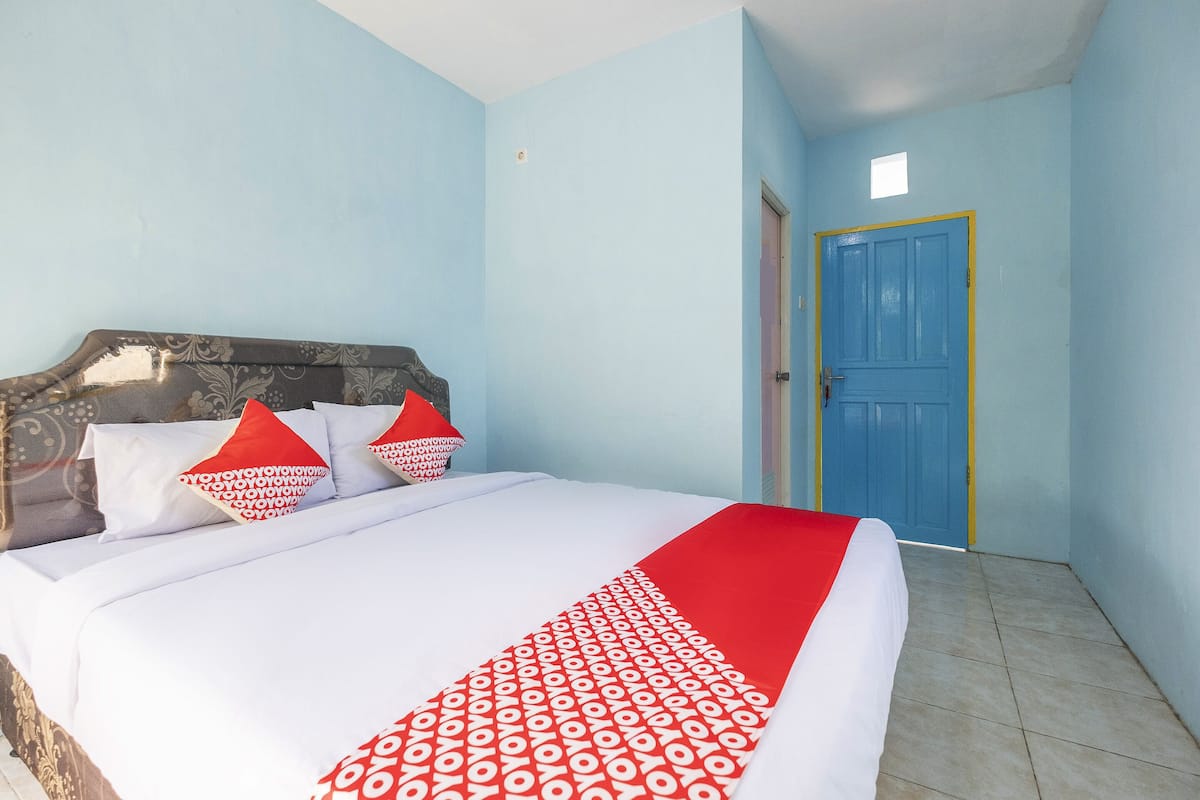 A bed with white bedding and red accents, a blue door, and light blue walls.