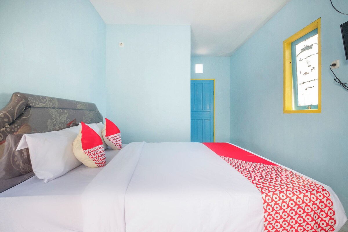 A bedroom with a bed, pillows, a blue door, and a window with a yellow frame.