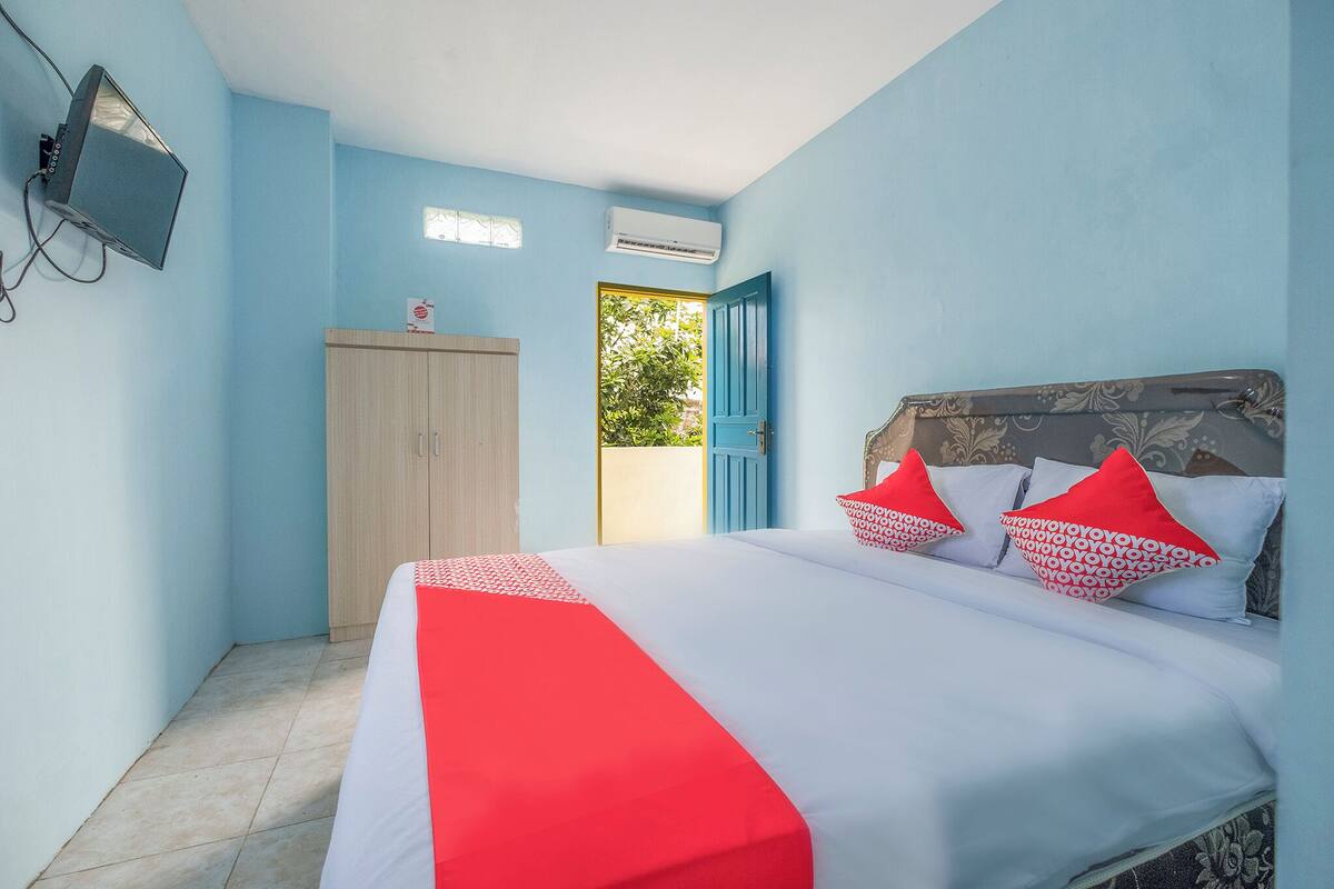 A bedroom with a bed, a wardrobe, an air conditioning unit, and a television.