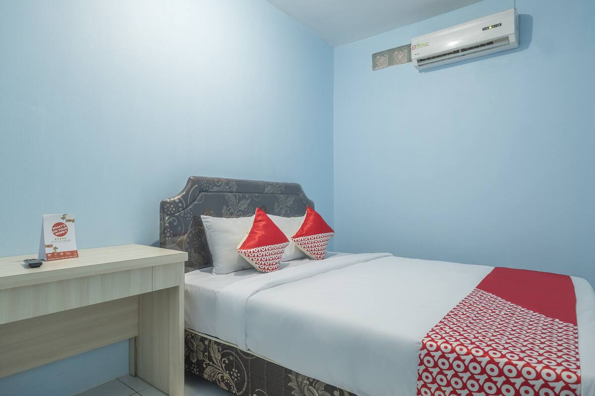 A bedroom with a bed, a nightstand, a red and white patterned bedspread, and a wall-mounted air conditioner.