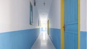 A long, narrow hallway with white and blue walls, a tiled floor, and a blue door with a yellow frame. - Hotel O RF Homestay (Makassar)