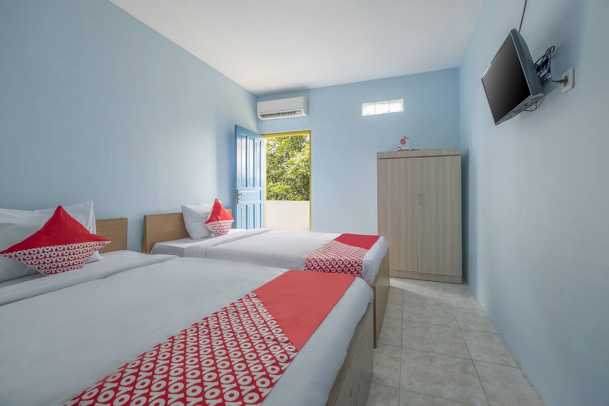 A hotel room with two beds, a TV, an air conditioner, and a wardrobe.