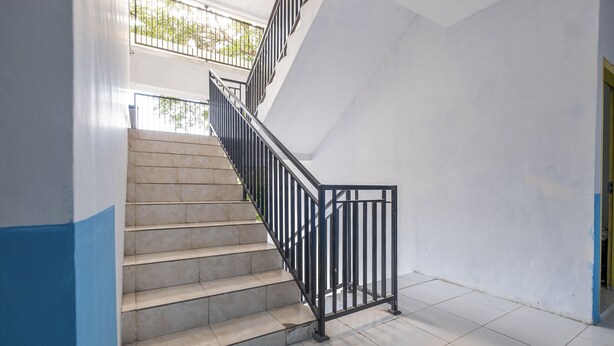 A staircase with a metal railing, white walls, and a tiled floor. - Hotel O RF Homestay (Makassar)