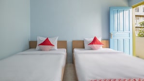 A room with two beds, each with white bedding and red pillows, a wooden headboard, and a blue door. - Hotel O RF Homestay (Makassar)