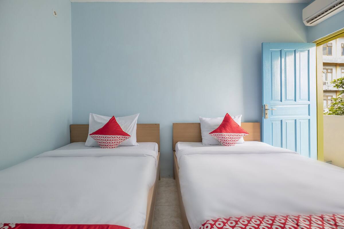 A room with two beds, each with white bedding and red pillows, a wooden headboard, and a blue door.