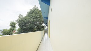 A narrow corridor with yellow walls and a tiled floor, leading to a building with a blue roof. - Hotel O RF Homestay (Makassar)