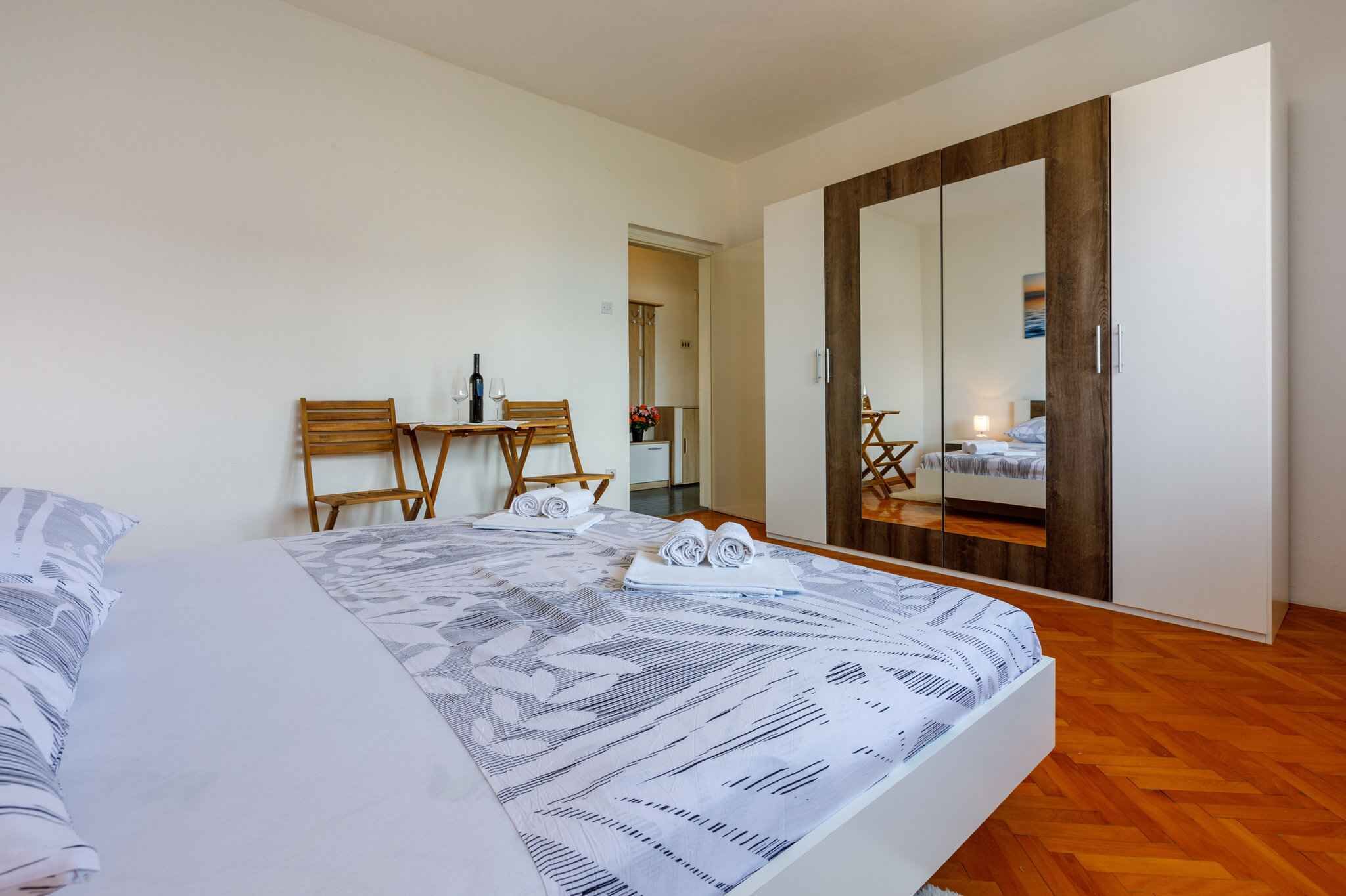 Ein Schlafzimmer mit einem großen Bett, einem Holzschrank, einem kleinen Tisch mit Stühlen und einem Spiegel.