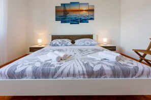 Ein ordentlich bezogenes Bett mit einem gemusterten Überwurf, zwei Nachttischlampen und einem an der Wand hängenden Sonnenuntergangsbild.