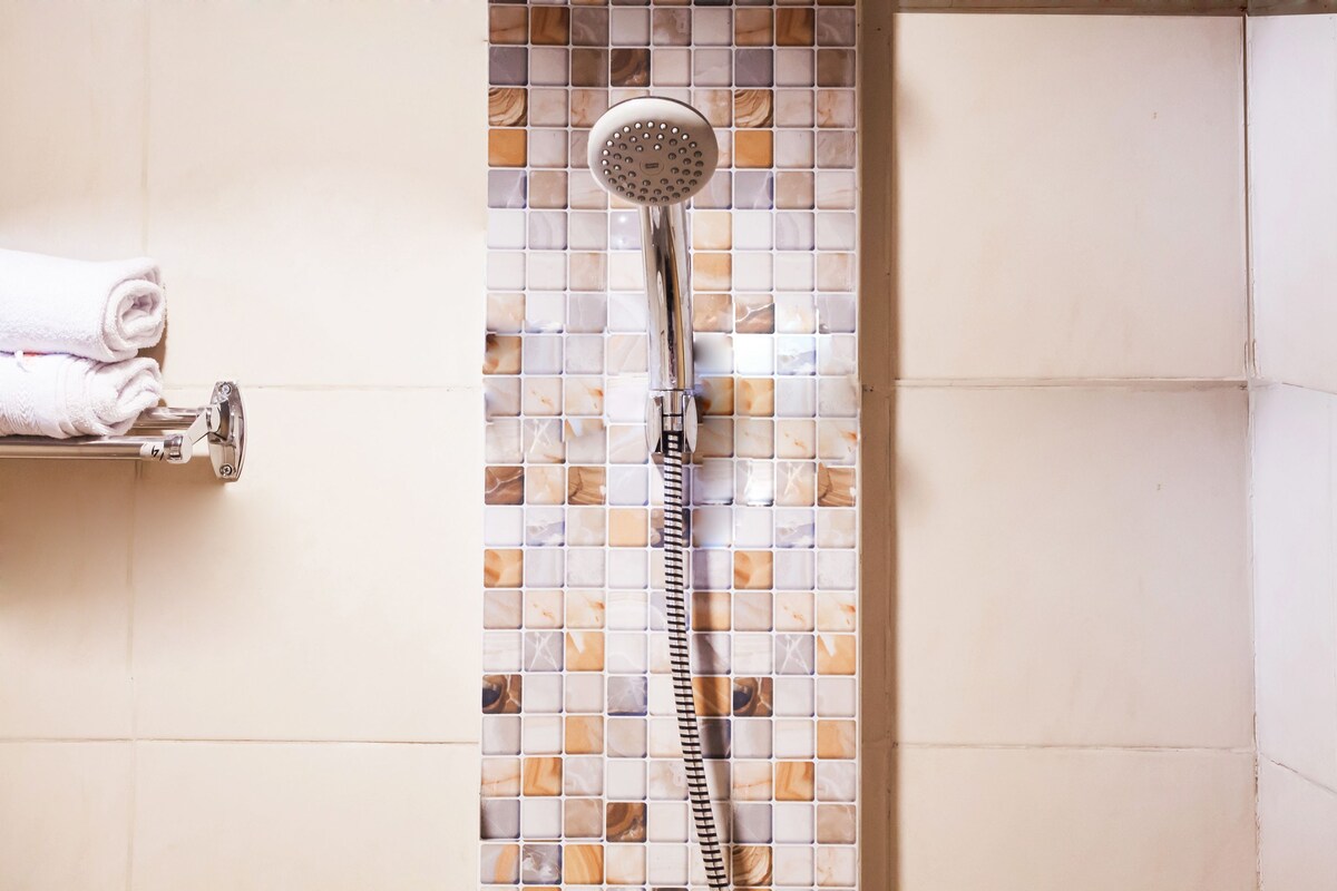 A shower with a handheld showerhead and a tiled wall.