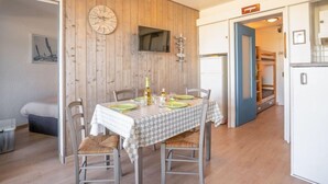 A dining area with a wooden wall, a clock, and a television. - Résidence du Golfe by Interhome (Port Camargue)