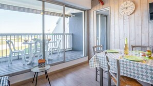 A dining area with a table set for two, a large window with a view, and a wooden wall with a clock. - Résidence du Golfe by Interhome (Port Camargue)