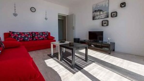 A modern living room with a red sofa, a black coffee table, a TV on a black stand, and a painting on the wall. - Holiday apartment mit Meerblick und Klimaanlage (Novi Vinodolski)
